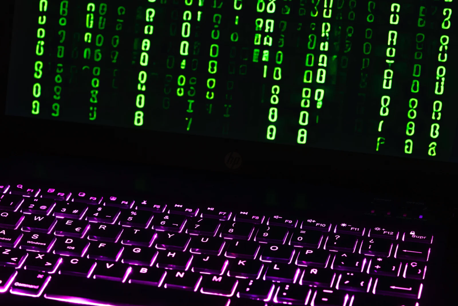 Illuminated laptop keyboard with Matrix-style green code cascading down screen.