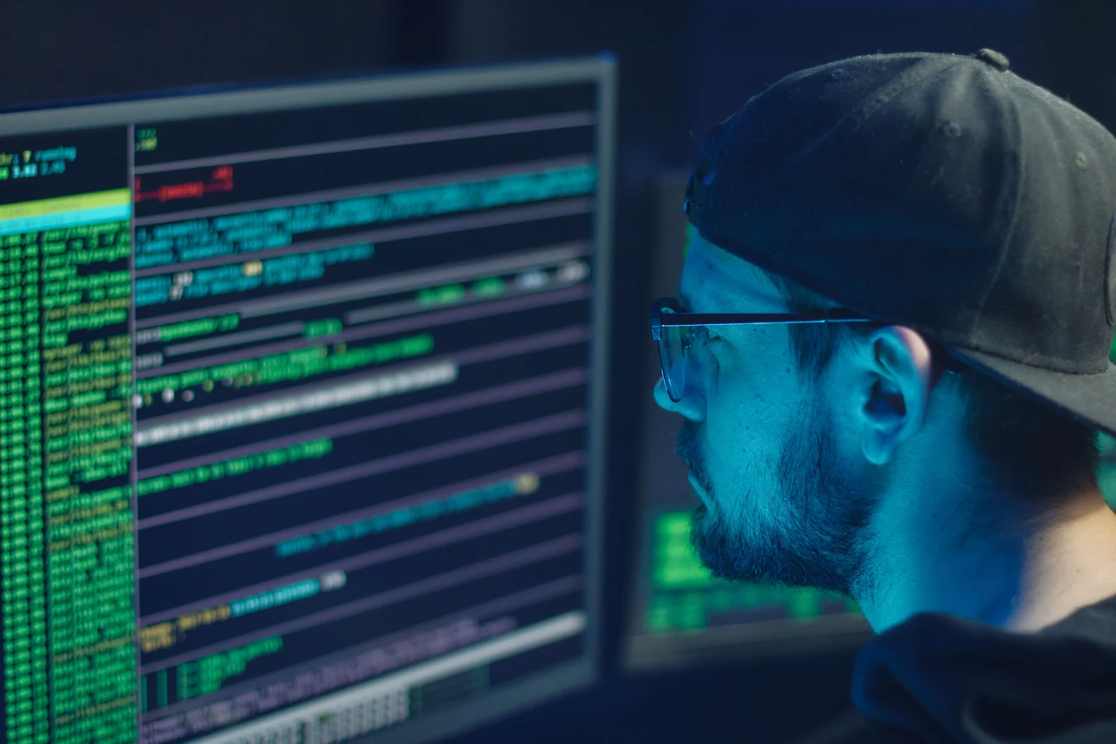 A cybersecurity expert inspecting lines of code on multiple monitors in a dimly lit office. A cybersecurity expert inspecting lines of code on multiple monitors in a dimly lit office.