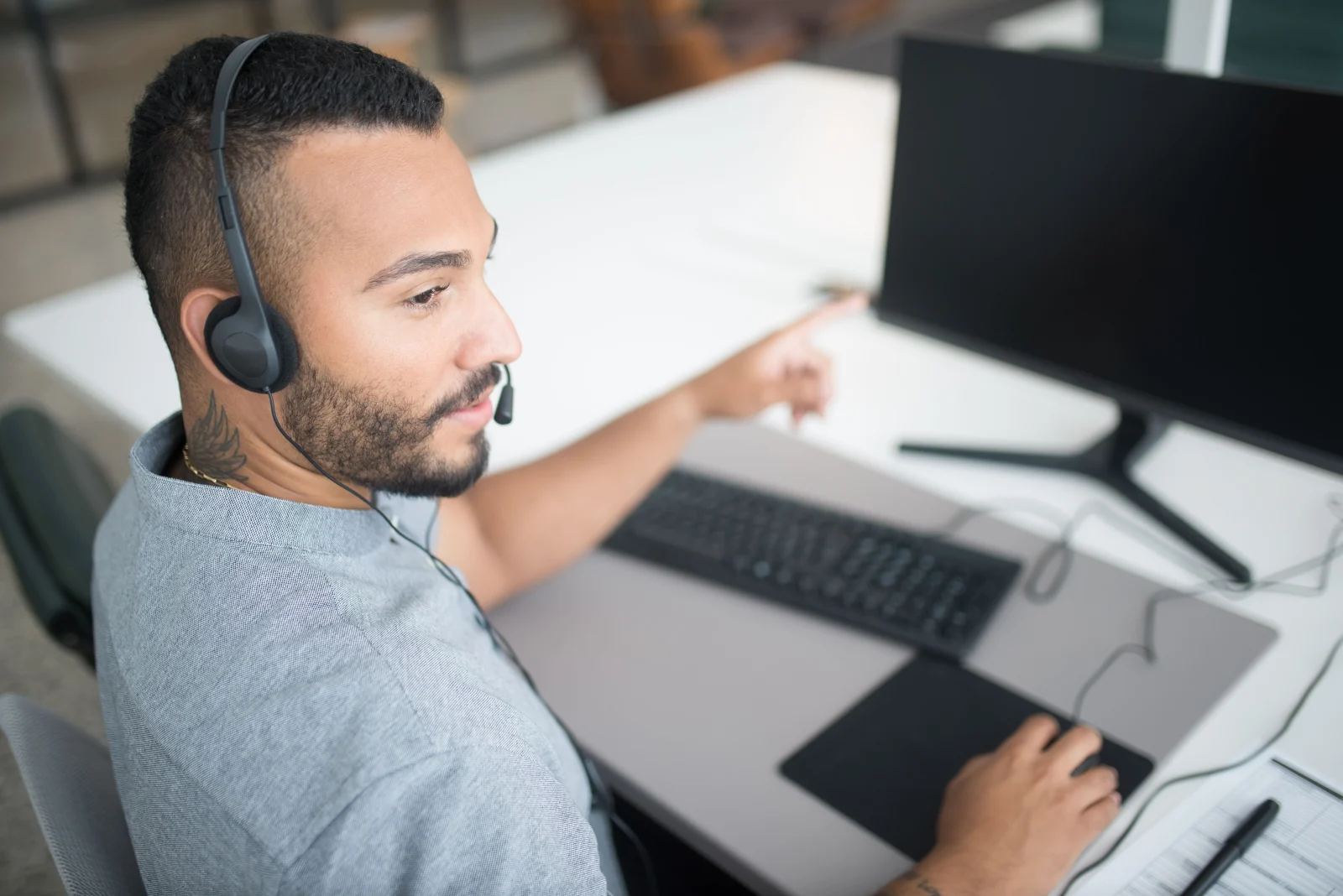 Customer service agent using a computer and headset within a modern office setting. Customer service agent using a computer and headset within a modern office setting.