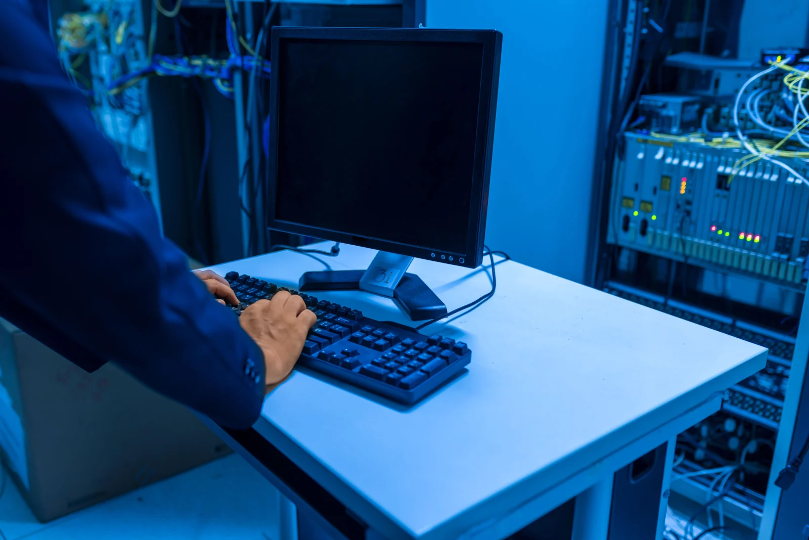 An IT professional operates a computer in a server room, managing network systems and connected devices. An IT professional operates a computer in a server room, managing network systems and connected devices.