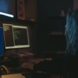 A woman working on programming tasks with multiple screens in a dimly lit room.