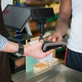 A customer making a payment with a credit card at a store checkout counter using a card reader.