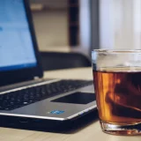 A comforting workspace featuring a laptop and a hot glass of tea on a wooden desk.